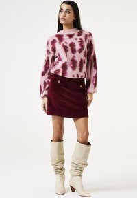 Pull en relief rose et bordeaux avec motif léopard ; jupe mini en velours côtelé bordeaux ; bottes crémeuses à bout pointu, à l'aspect décontracté, arrivant au genou.