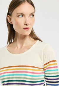 Chemise à manches longues couleur crème avec des rayures horizontales orange, jaune, rose, bleu-vert, vert et violet. Encolure ronde, texture douce.