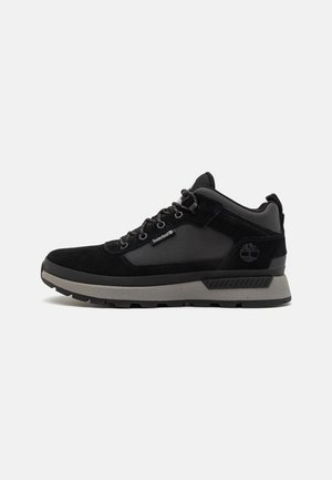Zapatilla Timberland de corte medio en negro y gris con cierre de cordones, cuello acolchado y logotipo de la marca en el lateral y la lengüeta.