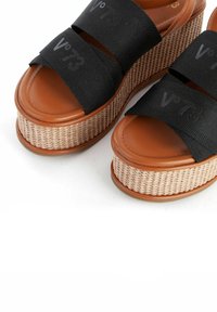 Sandali platform neri con basi in paglia intrecciata. Le cinghie strutturate presentano un logo. Le solette imbottite marroni offrono comfort.