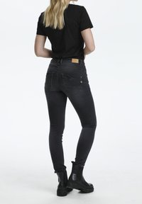 Jean noir taille haute avec une coupe slim, poches arrière plaquées et détails de couture subtils, associés à des bottines noires.