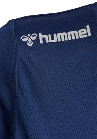 Granatowa koszulka sportowa z fakturowanej tkaniny. Zawiera białe logo "hummel" na prawym ramieniu. Krótkie rękawy i dopasowany krój.