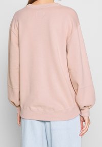 Jasnoróżowy, oversize'owy sweter z długimi, marszczonymi rękawami i okrągłym dekoltem. Miękki materiał z widocznymi detalami szycia.