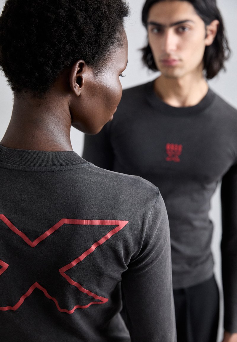 Langarmshirt in schiefergrau mit einem roten geometrischen Logo auf dem Rücken und einem kleineren Logo auf der Vorderseite. Weicher Stoff und taillierte Passform.