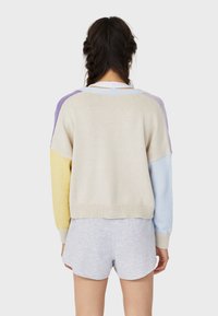 Wielokolorowy sweter z beżowymi, żółtymi, fioletowymi i niebieskimi sekcjami; miękka dziana tkanina, obniżone ramiona i prążkowany dół.