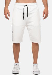 Shorts bianchi in cotone con elastico in vita e cordoncino, dotati di tasche laterali e dettagli neri sull'orlo e sui lati.