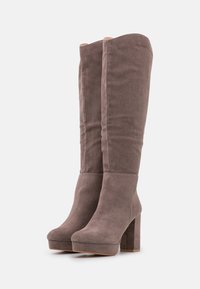 Botas de ante taupe hasta la rodilla con tacón cuadrado. Las costuras laterales están cosidas y la punta es redondeada. Textura suave y diseño de plataforma.