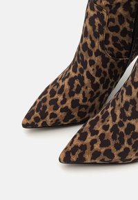 Bottines imprimé léopard avec un design à bout pointu, fabriquées en tissu avec une finition texturée, présentant des accents noirs et un détail de fermeture éclair.
