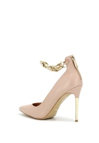 Pumps in vernice nudo con tacco alto, punta affusolata, cinturino alla caviglia in catena dorata e chiusura con zip sul retro, con un sottile tacco a stiletto metallico.