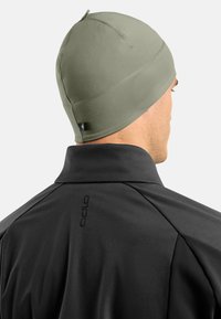 Casquette en tricot beige ajustée en tissu extensible avec une texture lisse. Veste noire à col montant avec un logo visible au dos.