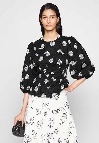 Top peplum preto com estampa floral branca, apresentando mangas bufantes e cintura franzida. Usado com uma saia branca exibindo um padrão floral preto.