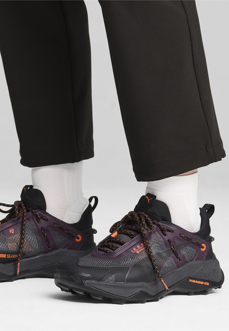 Must rämpär mustad ja lillad spordijalatsid on tekstuuriga disainiga, mesh-kihiga ja oranžide aktsentidega. Kinnised on oranžid koos peegeldava detailiga.
