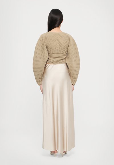 Beige textured long-sleeve top with gathered design, paired with a smooth satin cream skirt, ankle-length, and subtle sheen.