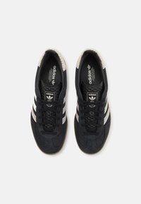 Zwarte suède sneakers met witte Adidas-strepen, gestructureerde stof op de teen, vetersluiting en een rubberen zool.