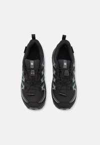 Zapatillas deportivas negras con parte superior de malla, acentos reflectantes y cordones elásticos; cuentan con un collar acolchado y suela de goma texturizada.