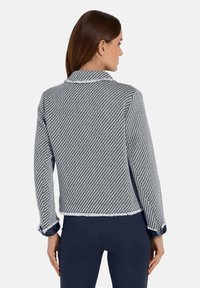Marineblauw en witte houndstooth jas met een korte snit, rafelige zoom en contrasterende manchetaccenten. Lange mouwen en klassieke kraag.