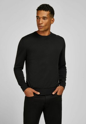 Pull en maille noire avec un col rond, des manches longues et des poignets côtes. Texture lisse, design ajusté et style minimaliste.