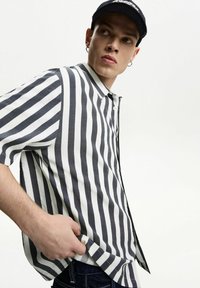 Striped short-sleeve shirt in gray and white with a buttoned collar. Features a relaxed fit and lightweight fabric. Worn with jeans.