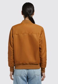 Giacca bomber marrone con polsini e orlo a coste, caratterizzata da un'esterno liscio e lucido e un design semplice, vista da dietro.