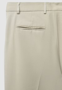 Pantalons beiges en matériau texturé, dotés d'une poche arrière unique et de passants de ceinture, avec une coupe ajustée et des détails de couture soignés.