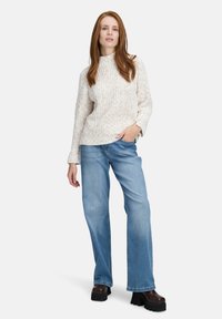 Light beige textured sweater with a high neck, paired with light blue wide-leg jeans. Model wears dark platform boots.