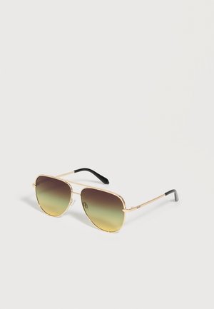 Lunettes de soleil aviateur à monture dorée avec verres dégradés marron-jaune et branches noires sur fond blanc.
