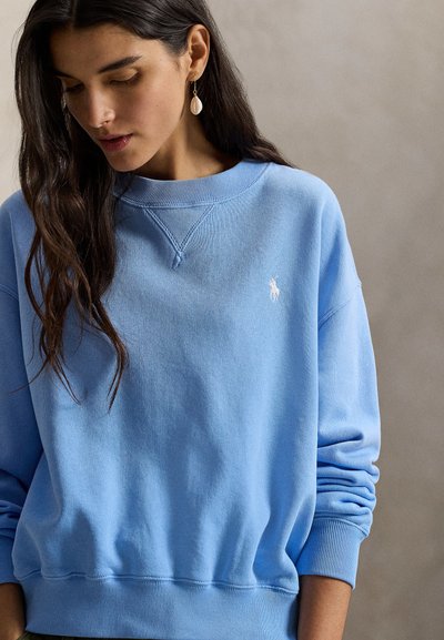 Ανοιχτό μπλε φούτερ με ριμπ μανσέτες και τελείωμα, με μικρό λευκό λογότυπο στο στήθος, κατασκευασμένο από απαλό βαμβακερό υλικό.