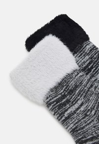 Calze pelose in bianco e nero con un risvolto superiore in soffice peluche. La parte principale presenta un motivo a maglia grigia testurizzata e una sezione bianca liscia e morbida.
