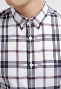 Wit en marineblauwe geblokte overhemd met bordeauxrode accenten, button-down kraag en witte knopen. Het materiaal lijkt glad met een evenwichtig patroonontwerp.