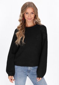 Pulover negru tricotat cu accente florale texturate pe umăr, decolteu rotund și croială lejeră. Asortat cu blugi din denim de culoare albastră deschisă.
