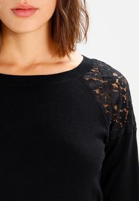 Czarny sweter z dzianiny z koronkowymi akcentami kwiatowymi na ramionach, prążkowanym dekoltem i miękką fakturą.