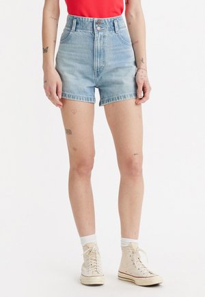 Světle modré šortky z denimu s vysokým pasem, s knoflíkovým zapínáním, designem pěti kapes a netradičním lemem. Spárovány s bílými teniskami s vysokým střihem.