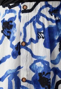 Bavlněná sukně s modro-černým abstraktním vzorem na bílém pozadí, s viditelnými knoflíky a strukturovanou tkaninou.