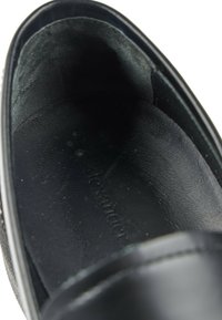 Vue rapprochée de l'intérieur d'un mocassin en cuir noir montrant la semelle intérieure texturée et une partie de l'ouverture de la chaussure.