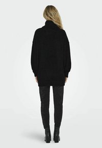 Maglione nero oversize con collo alto, realizzato in materiale soffice. Abbinato a pantaloni neri aderenti e scintillanti, insieme a stivaletti.