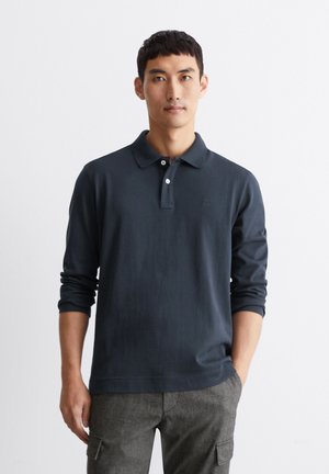 Navyblaues Langarm-Polohemd mit klassischem Kragen, Knopfleiste mit zwei Knöpfen und dezentem Logo-Detail, kombiniert mit grauen strukturierten Hosen.