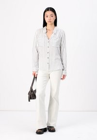 White striped button-up shirt with two chest pockets, paired with light flared pants and dark brown boots, holding a small brown bag.