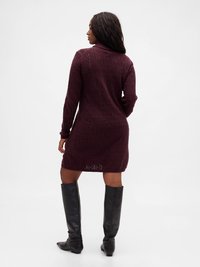 Rochie tricotată burgundy cu un model diamantat texturat, mâneci lungi și guler înalt. Asortată cu cizme negre din piele până la genunchi.