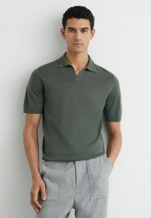 Tricou polo verde închis cu mâneci scurte și un guler mic, asortat cu pantaloni gri deschis, cu buzunare aplicate și țesătură texturată.