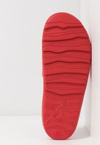 Suola di sneakers rossa con design testurizzato e ondulato. Presenta un logo Jumpman ben visibile vicino alla parte inferiore. Bordi lisci con punta arrotondata.