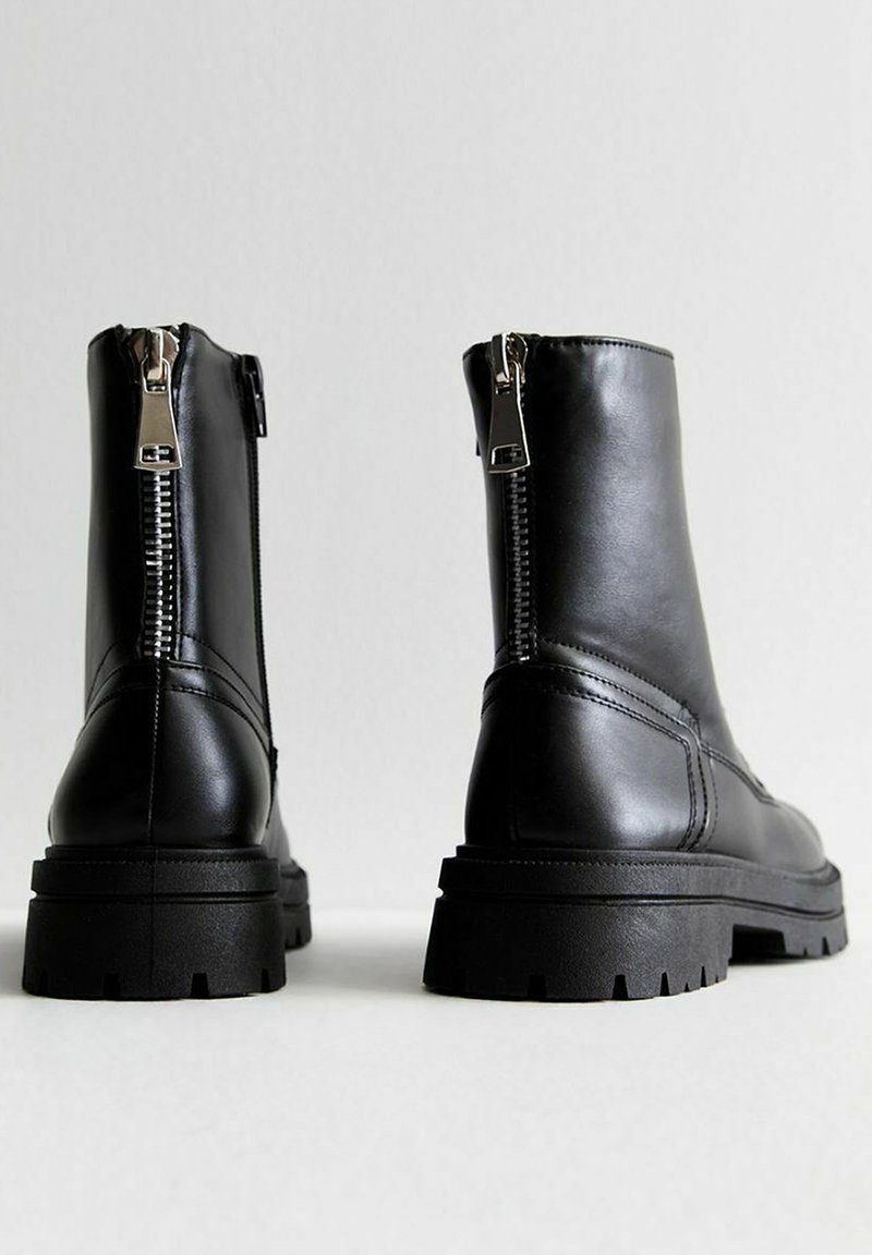 Stivali neri alla caviglia in pelle liscia. Presentano una zip laterale e una suola spessa e testurizzata con un motivo di battistrada distintivo.