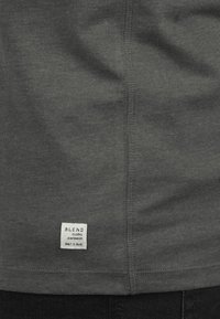 Donkergrijze katoenen t-shirt met een klein wit label met de tekst "BLEND" en zichtbare stikseldetails langs de zoom en de zijnaad.