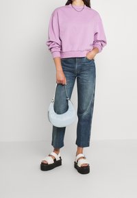 Felpa lilla, jeans blu a gamba dritta, sandali bianchi con piattaforma e una borsa a tracolla azzurro chiaro con dettagli argentati.