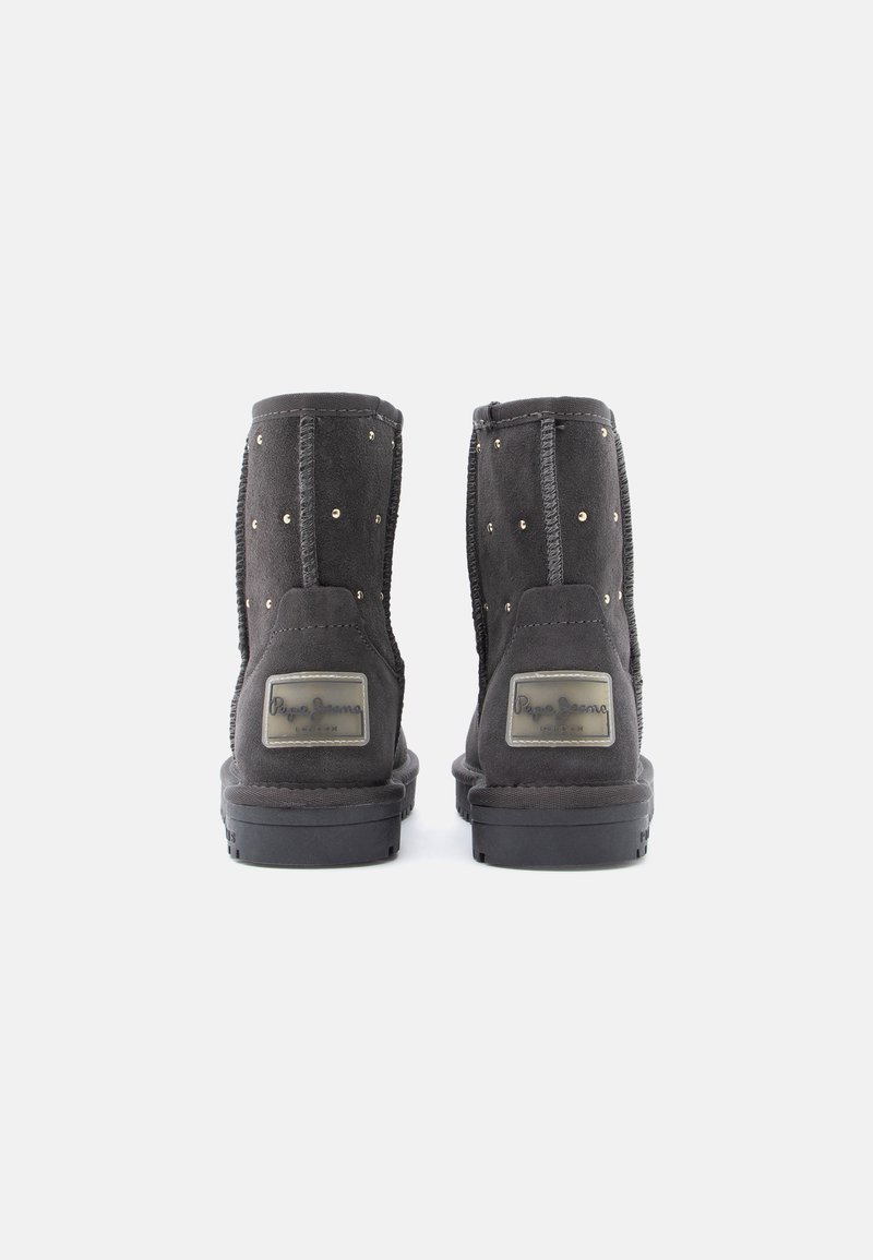 Schwarze Wildleder-Ankle Boots mit dekorativen goldenen Nieten, ausgestattet mit einer soliden Gummisohle und einem markierten Plakettendetail an der äußeren Ferse.