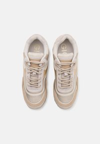 Zapatillas beige y marrones con una parte superior de malla texturizada, acentos de cuero en contraste, cordones redondos, cuello acolchado y logo dorado en la plantilla.