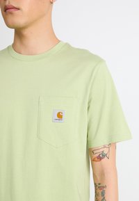 T-shirt en coton vert clair avec un col rond et une poche poitrine gauche ornée d'un patch rectangulaire du logo Carhartt.