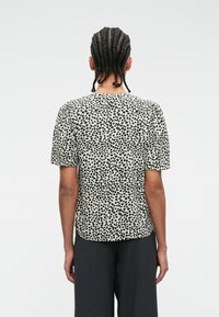 Μπλουζάκι κοντού μανικιού με κρεμ φόντο και μαύρο σχέδιο με στίγματα, φτιαγμένο από απαλό ύφασμα, με χαλαρή εφαρμογή και κυκλική στριφτή άκρη.