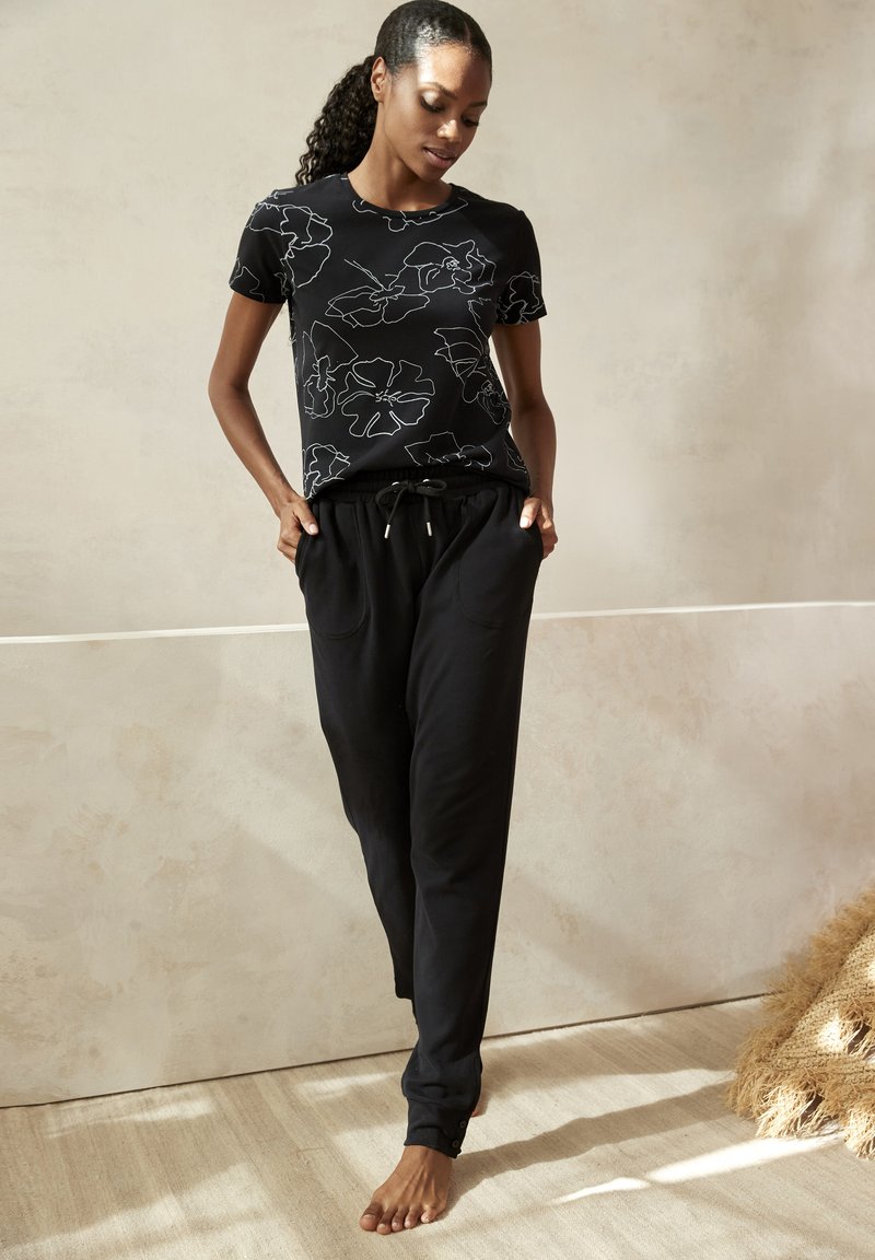 Camiseta negra con estampado de contorno floral blanco, combinada con pantalones negros de cuerda con bolsillos laterales y piernas ajustadas.