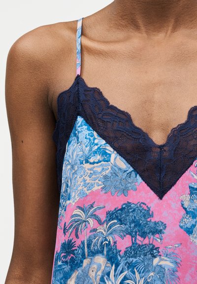 Γυναίκα που φοράει αμάνικο τοπ με λεπτές τιράντες, διακοσμημένο με μπλε δαντέλα και ροζ-μπλε τροπικό σχέδιο.