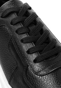 Zwarte lederen sneaker met een gestructureerde bovenkant, zwarte veters en een witte rubberen zool. Heeft gestikte details langs de zijkanten.